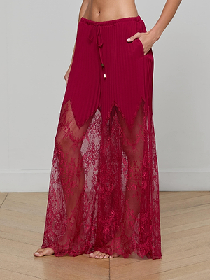 A person stands barefoot wearing the Sharon Cover-Up Pant—high-waisted, wide-leg red pants with pleated chiffon above the knee, sheer lace from mid-thigh to ankle, a drawstring waist, and side pockets.