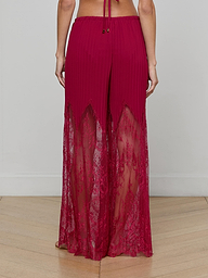 A person is shown from the back against a plain light background, wearing the Sharon Cover-Up Pant—high-waisted, wide-leg pants in red lace featuring sheer lace panels, a solid waistband, and a pleated upper section.