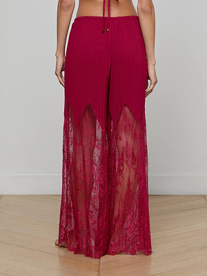 A person stands on a wooden floor with their back to the camera, wearing Sharon Cover-Up Pants—high-waisted magenta pants featuring solid fabric from waist to mid-thigh and sheer lace from mid-thigh to ankles.