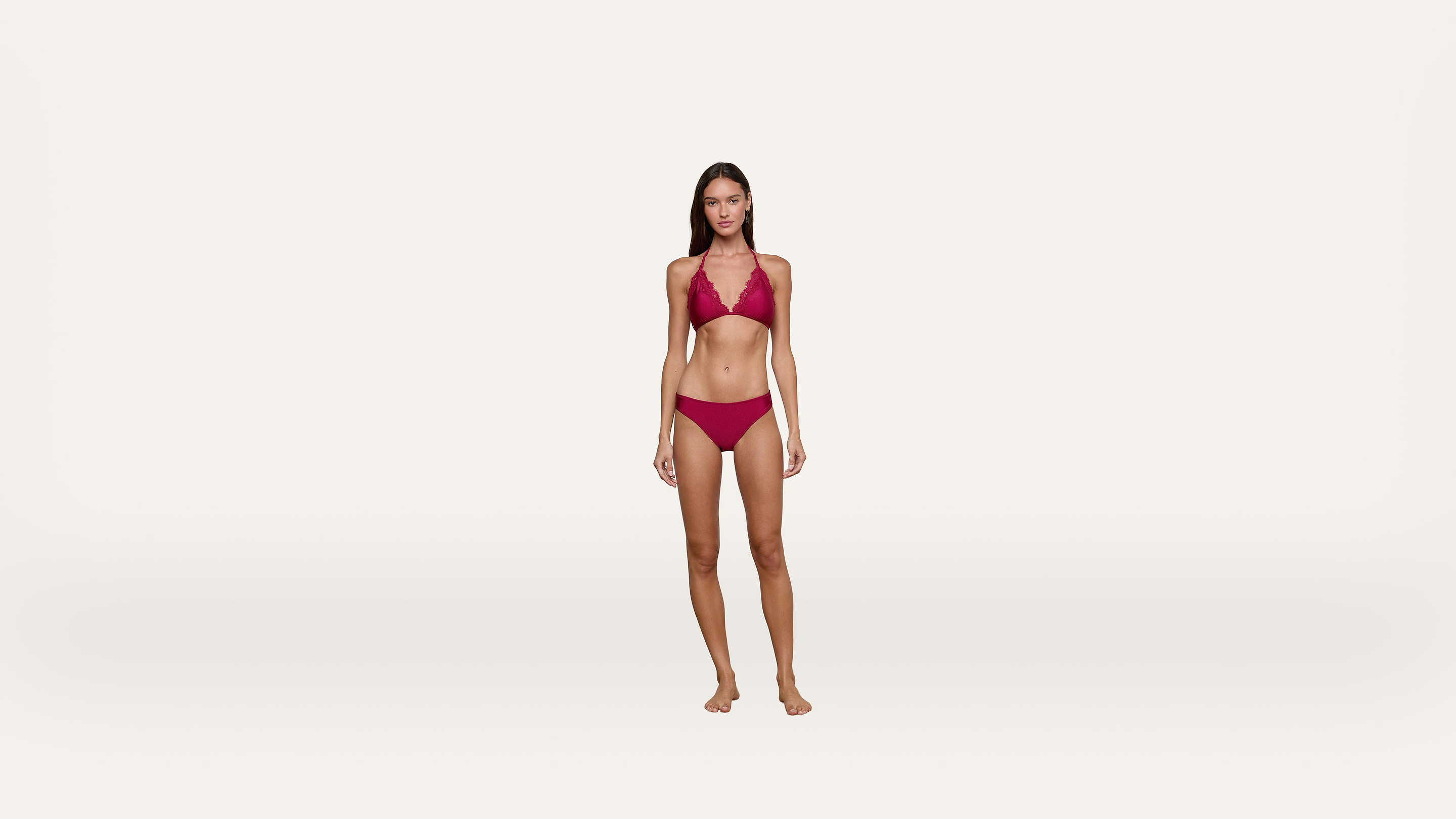 A woman stands barefoot against a plain white background, wearing a matching red bikini with a halter-style top and low-rise bottoms.