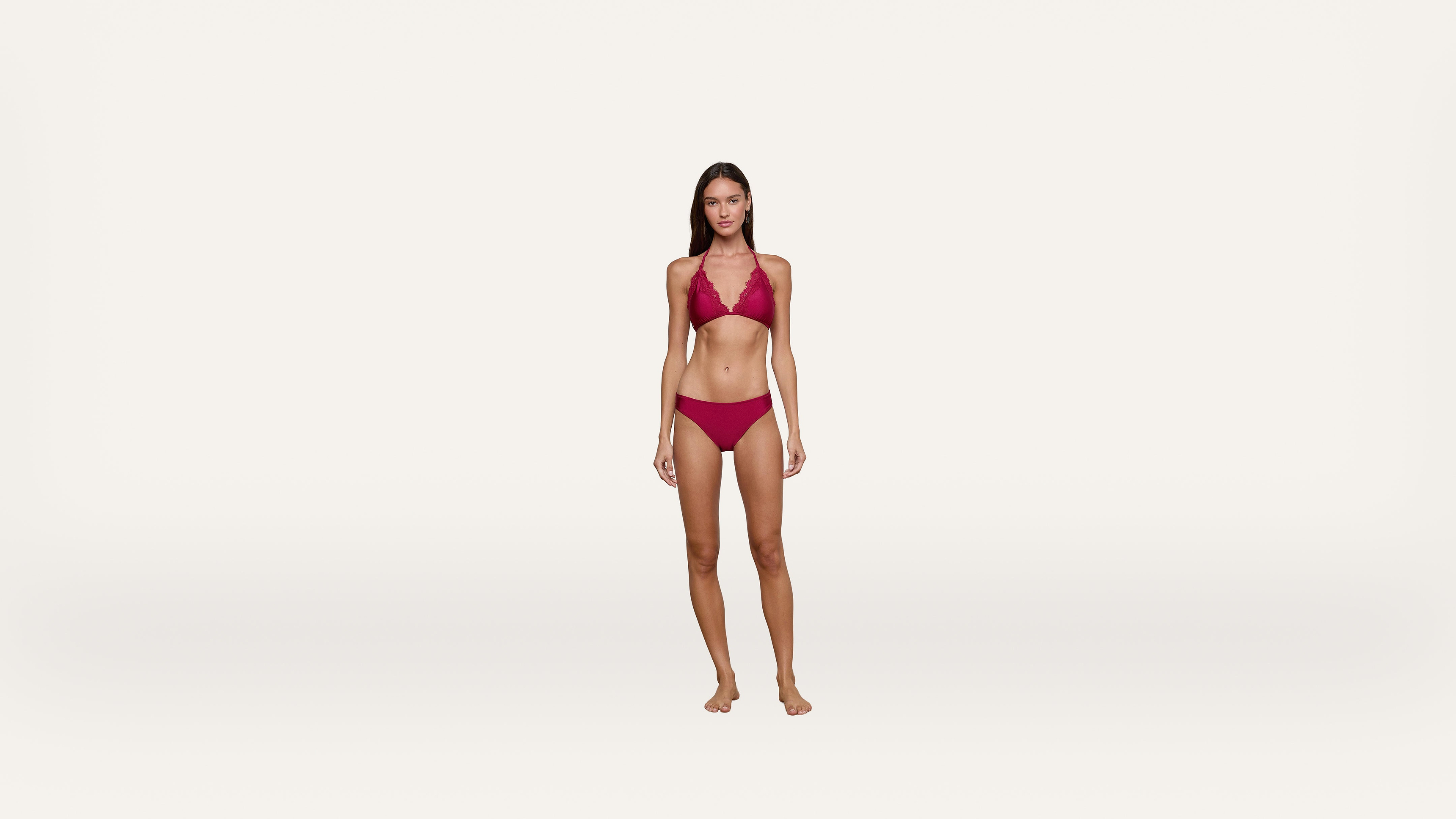 A woman stands barefoot against a plain white background, wearing a matching red bikini with a halter-style top and low-rise bottoms.