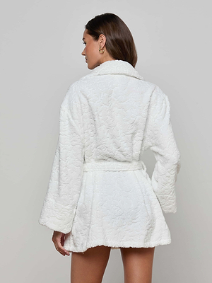 A woman faces away, wearing the Caterina Cover-Up Robe—textured white cotton jacquard with a belt and wide sleeves—against a plain light gray background.
