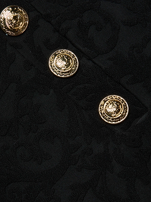 Close-up of the Coco Swim Skirt’s textured jacquard terry black fabric with a subtle floral pattern, accented by three shiny gold decorative buttons arranged diagonally.