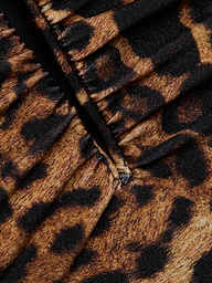 Close-up of gathered fabric from the Lilou One-Piece Swimsuit, showcasing its leopard print with brown and black spots and visible stitching down the center.