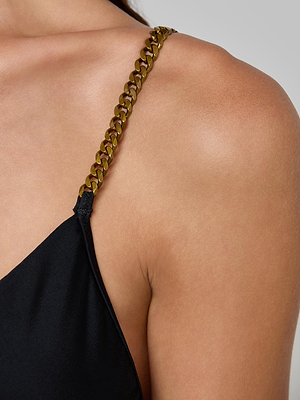 Close-up of a person’s shoulder wearing the Lilou One-Piece Swimsuit with a black fabric and gold chain strap, set against a neutral background. The image highlights the chain detail and smooth skin.