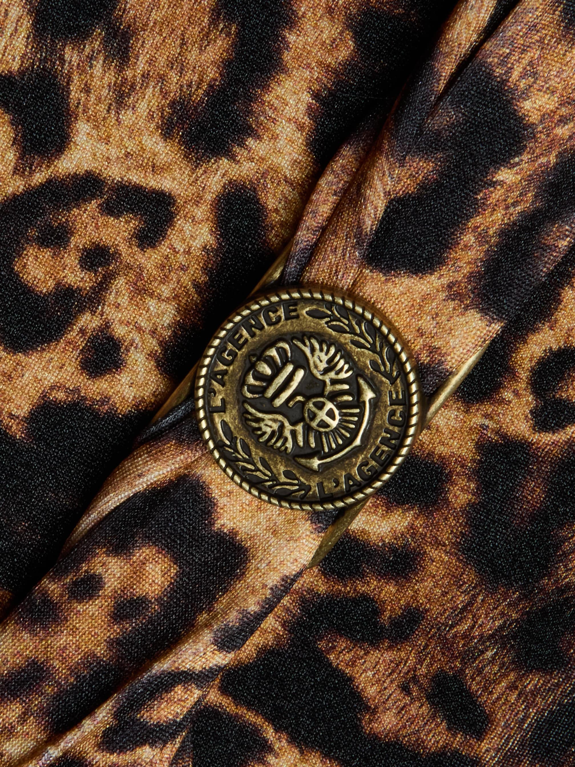Close-up of a brass L'AGENCE button with leaf detail, sewn onto brown and black leopard print fabric on the Lisa Plunge One-Piece Swimsuit.