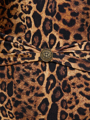 Close-up of the L'AGENCE Lisa Plunge One-Piece Swimsuit in leopard print, featuring a gold button with an embossed crown and laurel at the center, where the fabric gathers in a slight fold.