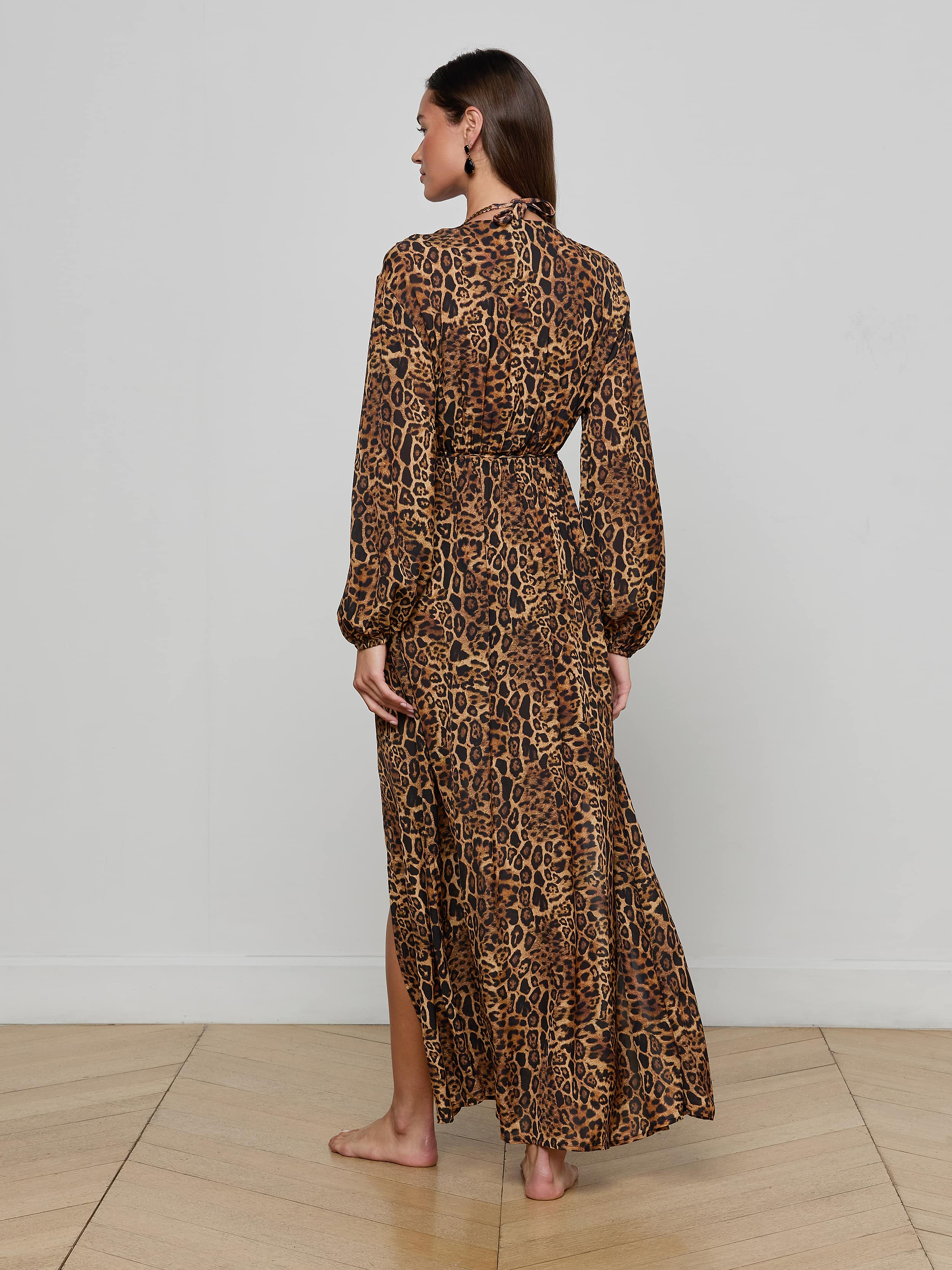 A woman stands barefoot, facing away, wearing the Sara Maxi Cover-Up Dress—an ankle-length, long-sleeve leopard print style—against a plain white background.