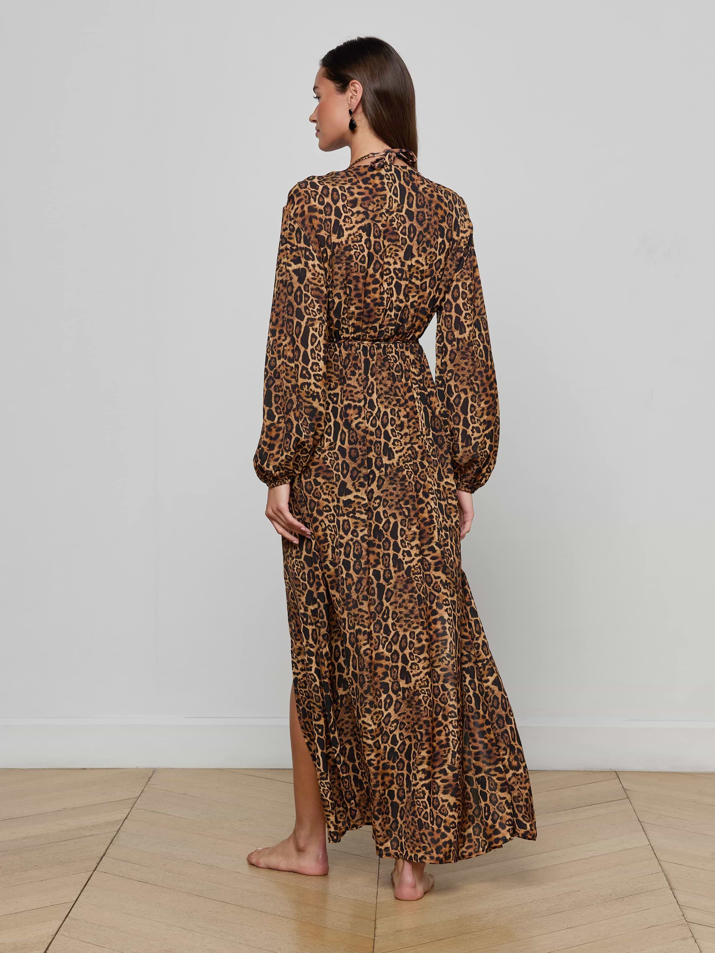 A woman stands barefoot, facing away, wearing the Sara Maxi Cover-Up Dress—an ankle-length, long-sleeve leopard print style—against a plain white background.