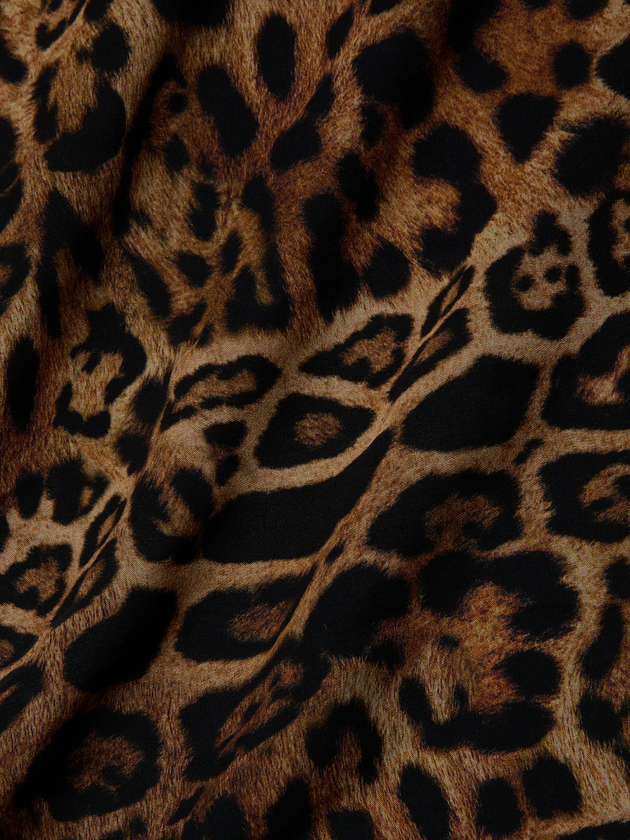 Close-up of the Sara Maxi Cover-Up Dress, showcasing its brown and black leopard print fabric with irregular shapes and spots reminiscent of wild animal fur—perfect for making a stylish statement.