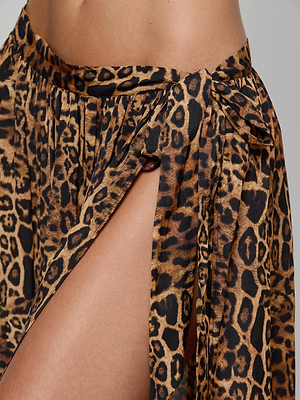 Close-up of a person wearing the Klaire Cover-Up Skirt by L'AGENCE, a high-slit leopard print wrap with a decorative waist tie, revealing part of their bare thigh and hip.