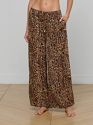 A person wearing the Geraldine Cover-Up Pant—a loose, wide-leg style with a brown and black leopard print and a comfortable pull-on fit—stands barefoot against a plain white background, embodying effortless resort wear.