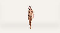 A woman stands against a plain white background wearing a leopard print bikini, looking forward with arms relaxed at her sides.