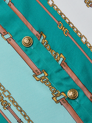 Close-up of the Wrena Cover-Up Dress by L'AGENCE, crafted from lightweight teal and light blue viscose with gold buttons. Features brown and gold chain and belt patterns—ideal as chic resort wear or a stylish beach cover-up.