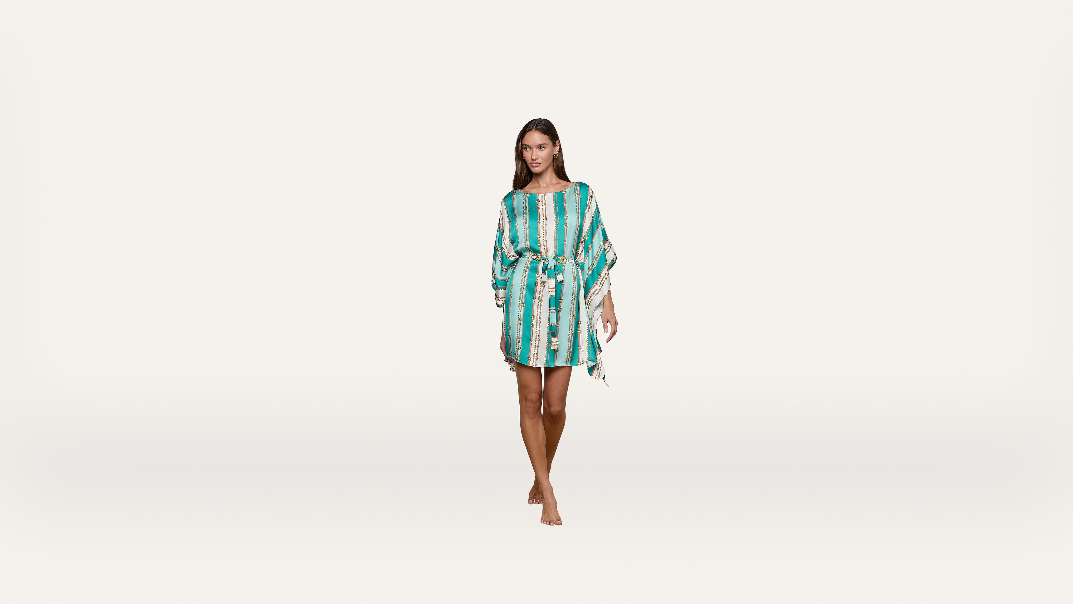 A woman in a turquoise and white striped dress with a belt walks barefoot against a plain white background.