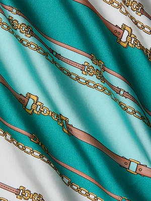 A close-up of fabric with a teal and white background shows a belt-stripe print of gold chains and brown leather belts, perfect for the stylish Alia Cover-Up Tunic.