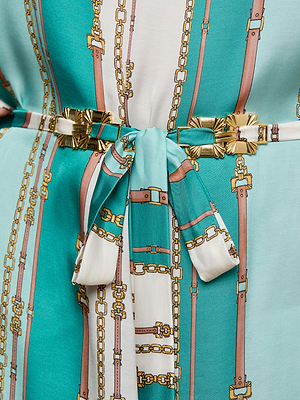 Close-up of the Alia Cover-Up Tunic in turquoise and white, featuring a belt-stripe print with gold chain and belt motifs, tied at the waist with a matching fabric belt and finished with gold decorative accents.