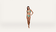 A woman in a green bikini stands confidently against a plain white background, posing with one hand on her hip and the other relaxed by her side.