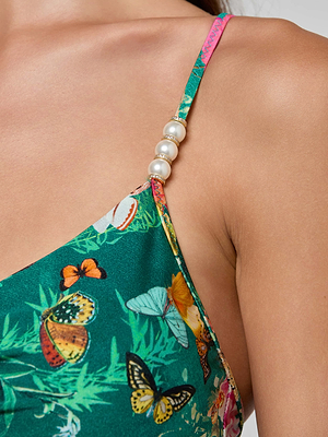 Close-up of a woman's shoulder wearing the Lilou One-Piece Swimsuit, which features a green floral-butterfly and leaf print and has a strap adorned with three pearl-like beads.