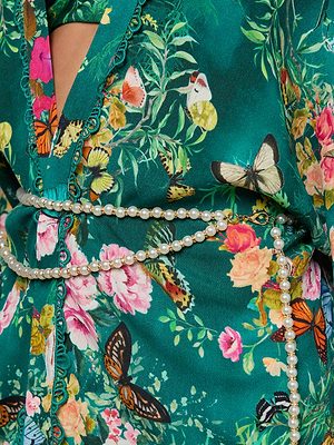 Close-up of the Caterina Cover-Up Kimono in vibrant green, adorned with pink, yellow, and orange flowers plus colorful butterflies. A double-strand pearl belt sits atop floral crochet trim for an elegant touch.