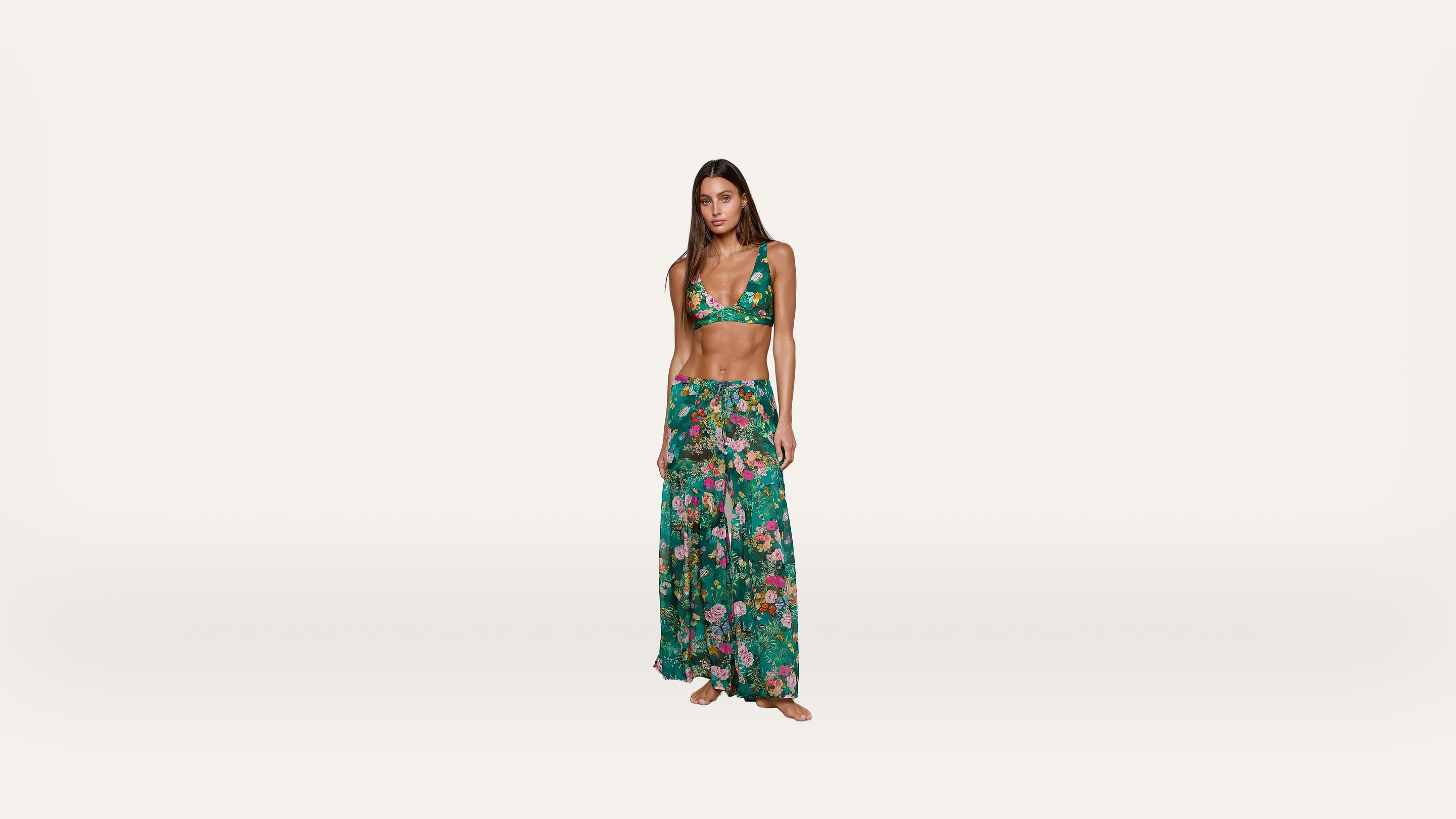 Woman wearing a green floral bikini top and matching long skirt standing barefoot against a plain white background.