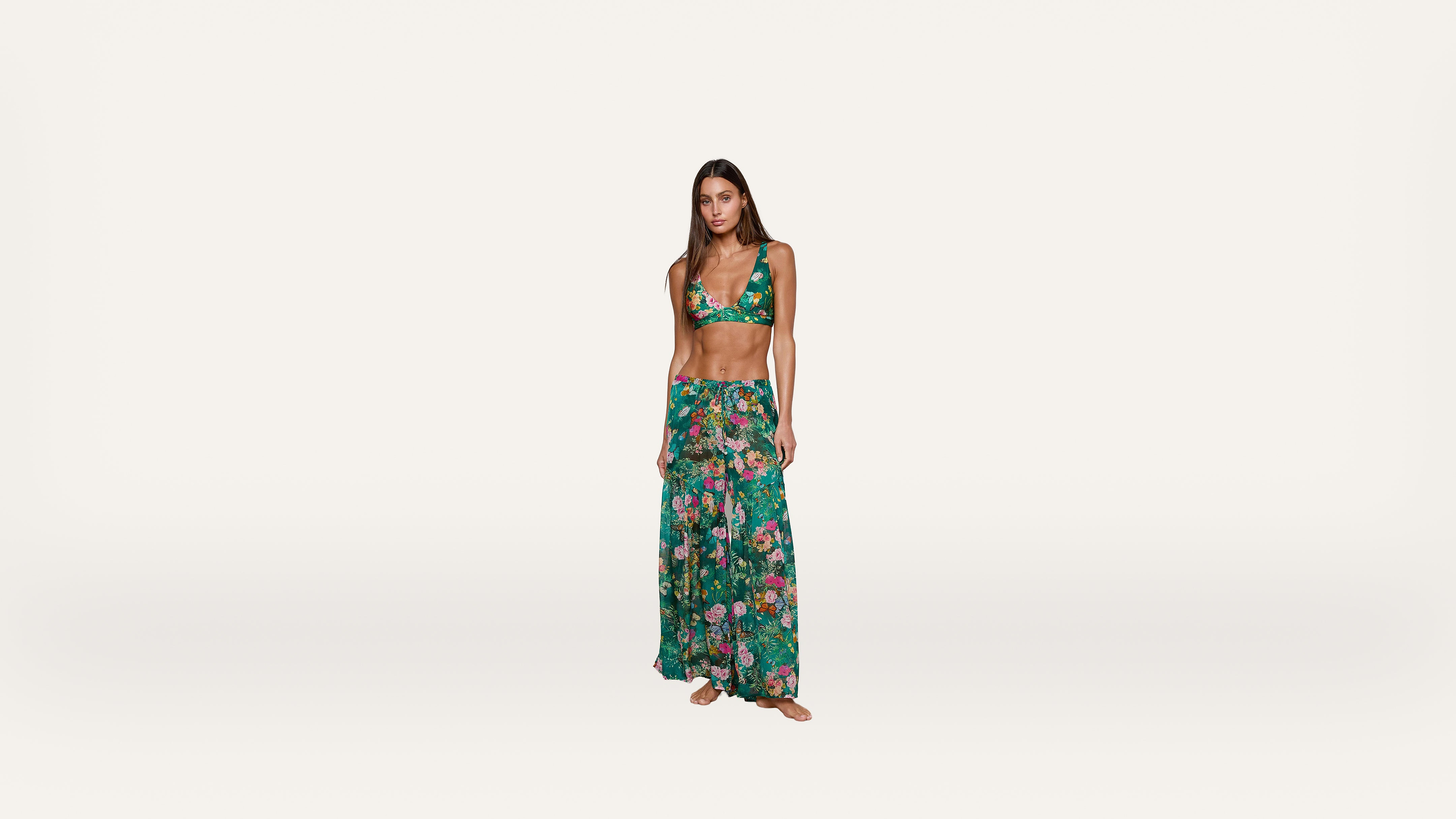 Woman wearing a green floral bikini top and matching long skirt standing barefoot against a plain white background.
