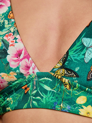 Close-up of the Lexie Bikini Top by L'AGENCE, a green secure-fit design with a deep V neckline and bold butterfly floral print, shown on a light-skinned model.