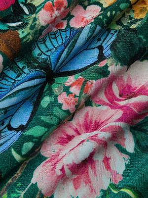 Close-up of the Lilou One-Piece Swimsuit, showing blue butterflies and vibrant pink flowers on a green leafy background. The fabric’s texture and folds are visible.