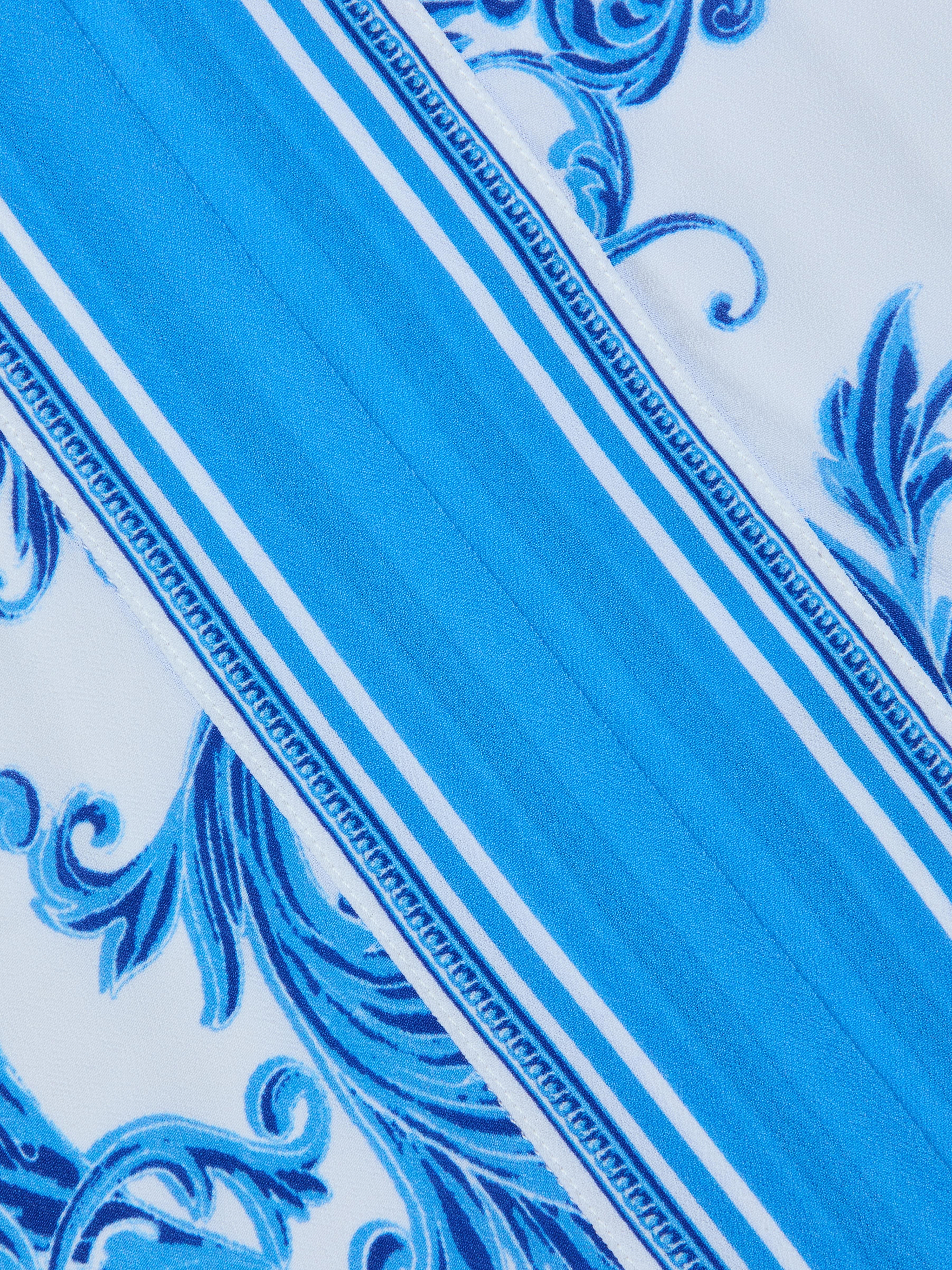 The Kara Kimono Cover-Up features blue and white diagonal stripes accented with ornate blue floral and vine patterns. Crafted from water-safe viscose crepe, its decorative trim borders the flowing design, set against a mostly white background highlighted by intricate blue details—making it a perfect blue baroque-inspired cover-up.
