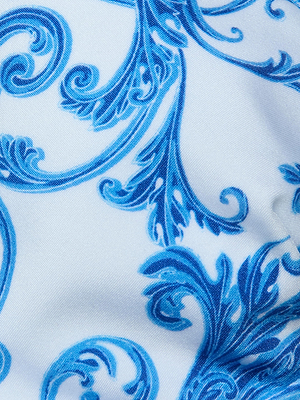 Close-up of the Lexie Bikini Top's white fabric, showcasing an intricate swirling blue baroque print with soft shadows and gentle folds.