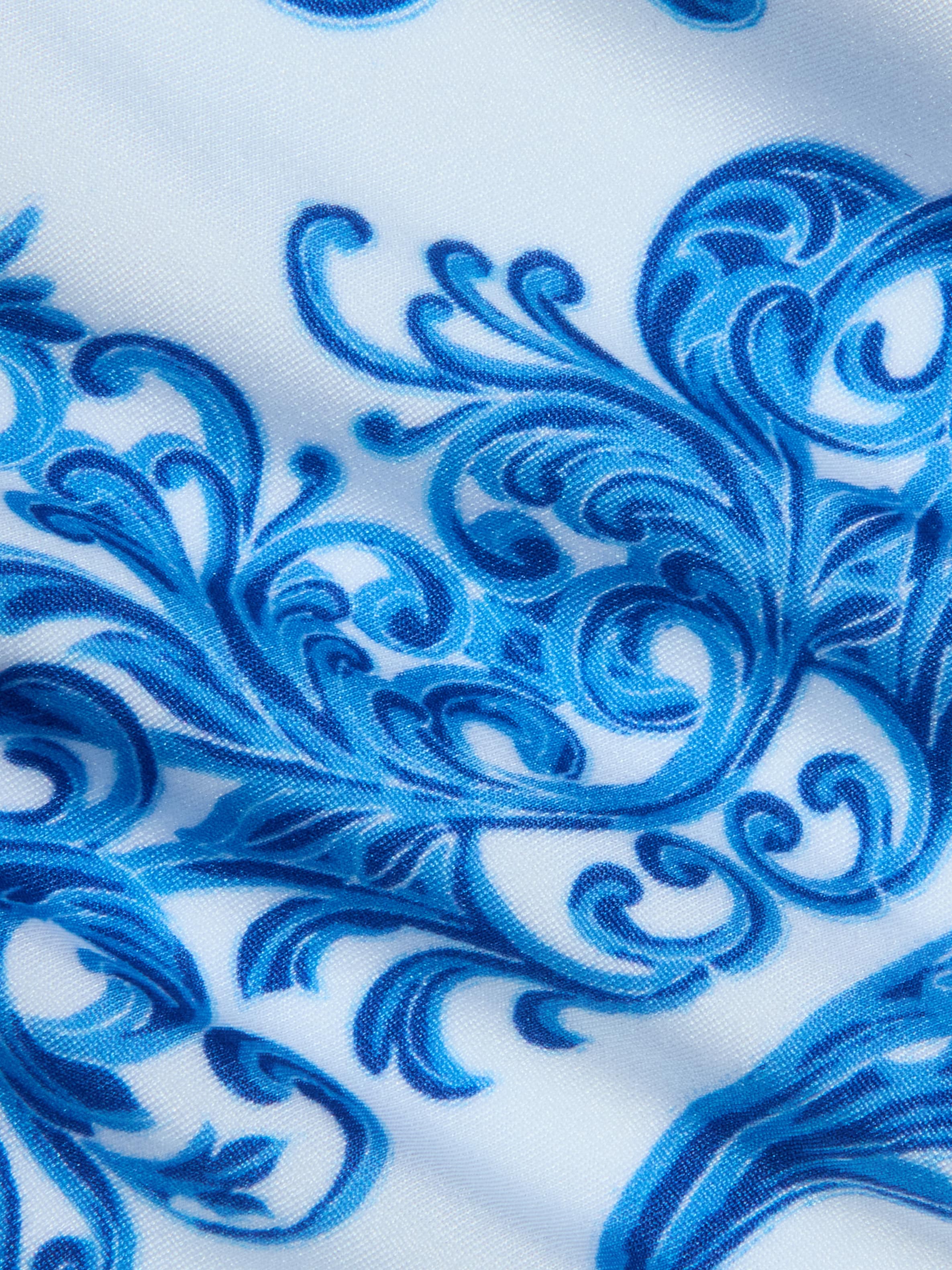 The Gianna Brazilian Bikini Bottom features a blue baroque print swirling with intricate floral, leaf, and vine-like designs over white fabric, creating a decorative and ornate look—perfect for a cheeky or Brazilian-style fit.