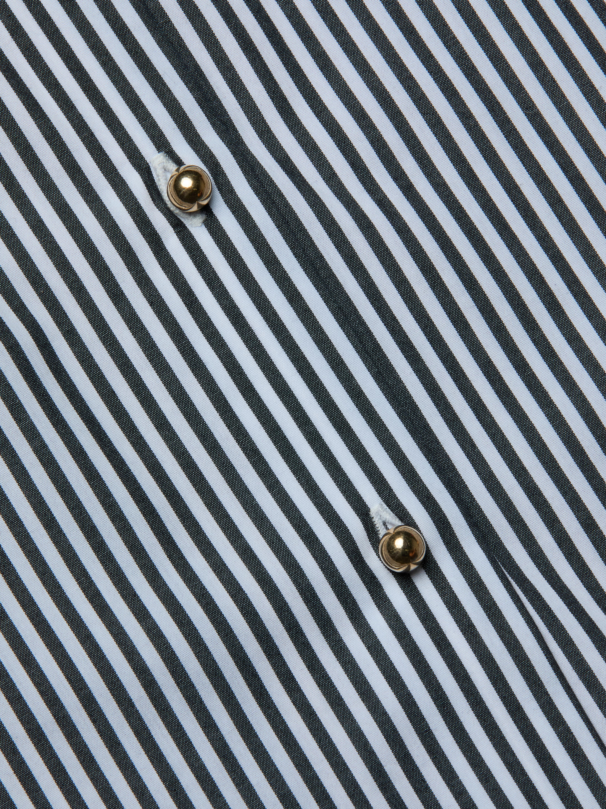 Close-up of the Lorena Cover-Up Shirt, showcasing its cotton poplin fabric with black and white diagonal stripes and two gold buttons sewn in a vertical line. The visible texture and stitching around the buttons highlight the crisp finish reminiscent of a classic resort shirt.