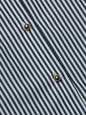 Close-up of the Lorena Cover-Up Shirt, featuring diagonal black and white vertical stripes and two shiny gold buttons. The uniform pattern and evenly spaced buttons add sophistication to this resort collection piece.