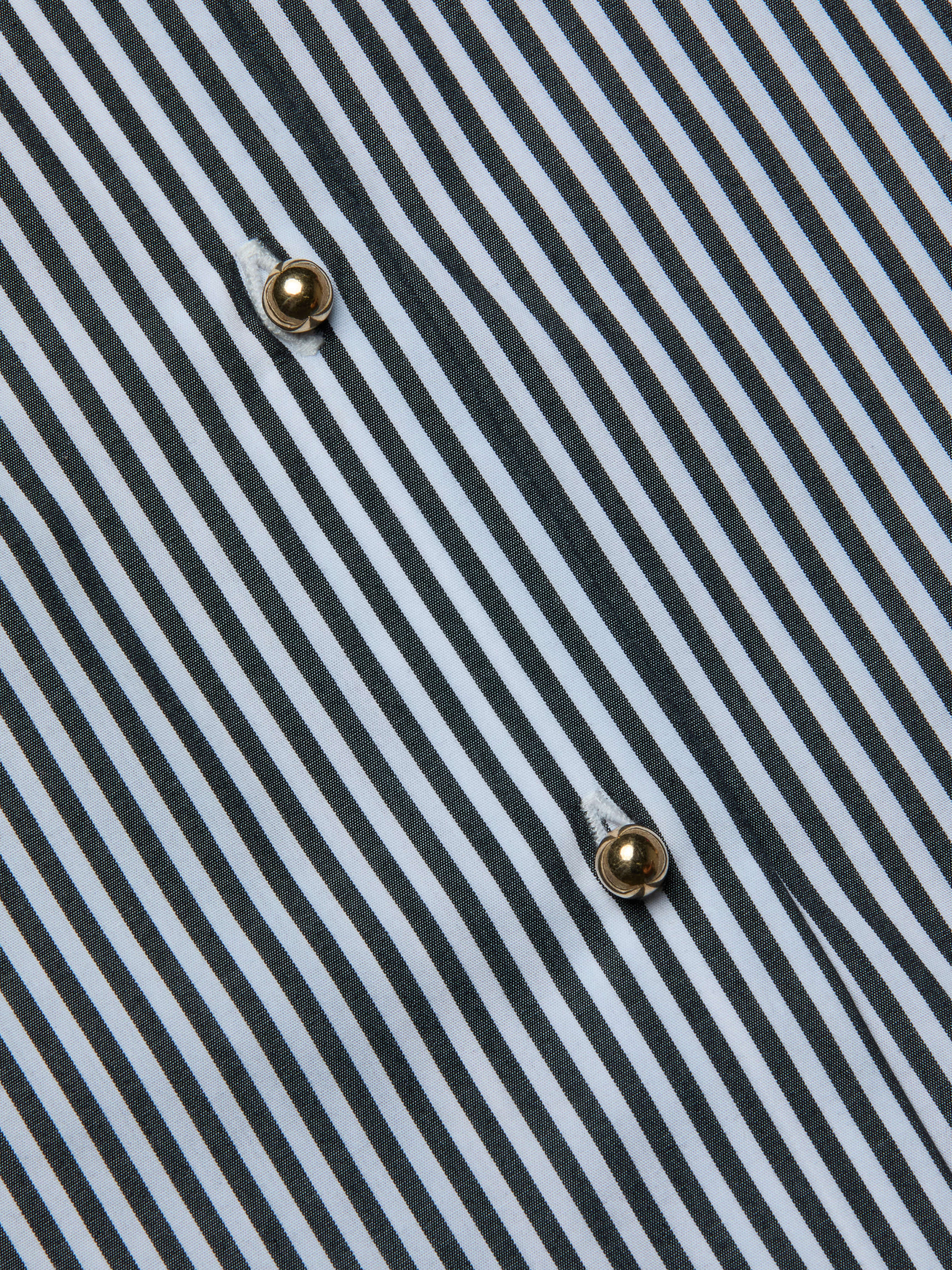Close-up of the Lorena Cover-Up Shirt, showcasing its cotton poplin fabric with black and white diagonal stripes and two gold buttons sewn in a vertical line. The visible texture and stitching around the buttons highlight the crisp finish reminiscent of a classic resort shirt.