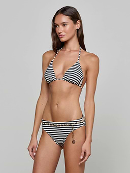 A woman wearing the Kristin Triangle Bikini Top, featuring black and white stripes and gold chain detail on the bottom, stands against a plain light background, embodying French Riviera swimwear style.