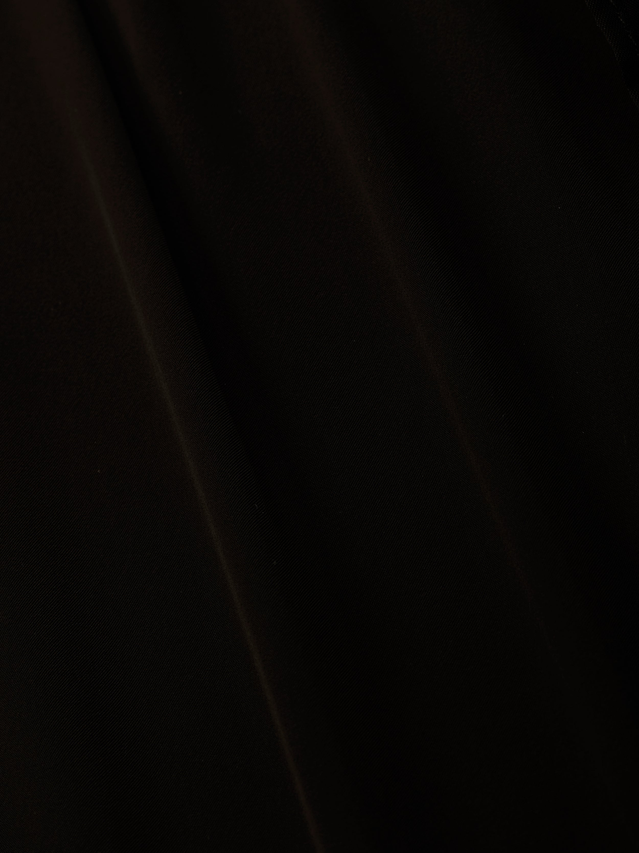 A close-up of black sheer chiffon fabric with subtle folds and soft diagonal shadows, perfect for the elegant Adonis Cover-Up Pant or a chic poolside look.