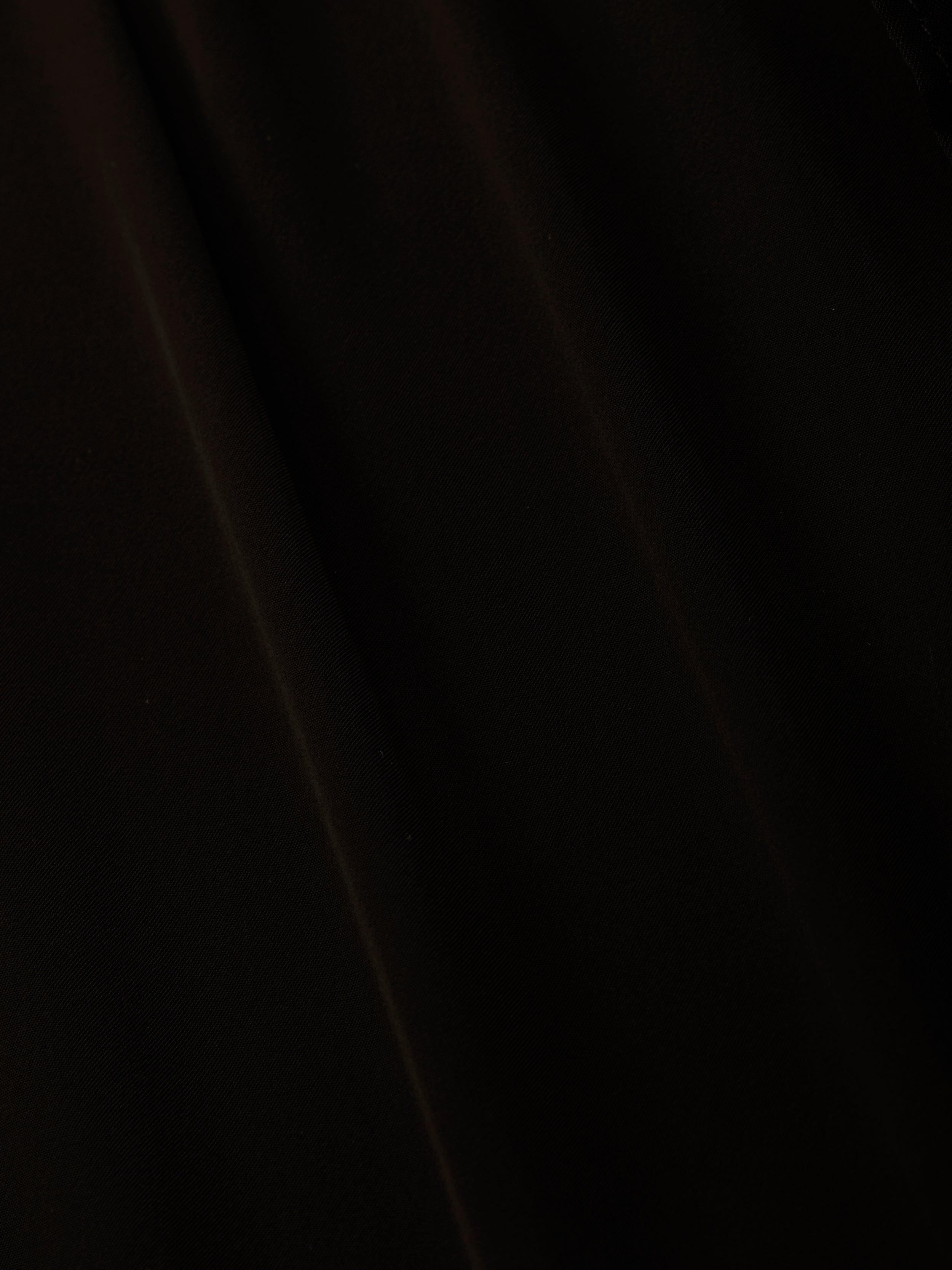 A close-up of black sheer chiffon fabric with subtle folds and soft diagonal shadows, perfect for the elegant Adonis Cover-Up Pant or a chic poolside look.