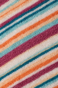 Close-up of the Lee Cover-Up Poncho, showcasing colorful, textured fabric with diagonal stripes in shades of purple, orange, teal, and white. The woven material evokes the soft and cozy feel of terrycloth—ideal for poolside lounging or relaxing after a swim.