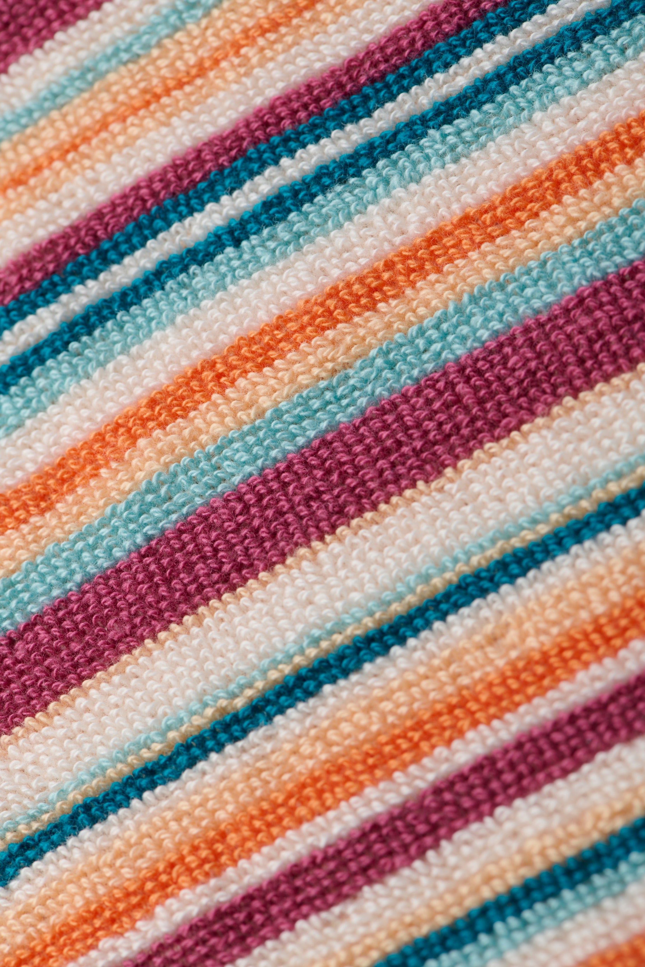 Close-up of the Lee Cover-Up Poncho, showcasing colorful, textured fabric with diagonal stripes in shades of purple, orange, teal, and white. The woven material evokes the soft and cozy feel of terrycloth—ideal for poolside lounging or relaxing after a swim.
