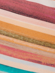Close-up of the Britt Tie-Side Bikini Bottom, showcasing textured horizontal stripes in shades of red, pink, orange, yellow, green, and beige. Designed with adjustable tie sides and moderate coverage, the fabric has a painted or printed appearance.