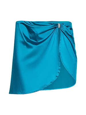 The Coco Mini Skirt Cover-Up is a shiny turquoise satin mini with a wrap front, gathered at the side by a silver brooch. Its asymmetrical hem and teal liquid shine make it an ideal chic bikini cover-up.