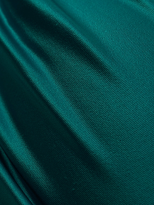 Close-up of emerald green satin fabric with a smooth, lustrous texture and gentle folds, evoking the luxurious sheen of the Krysta Halter Bikini Top.