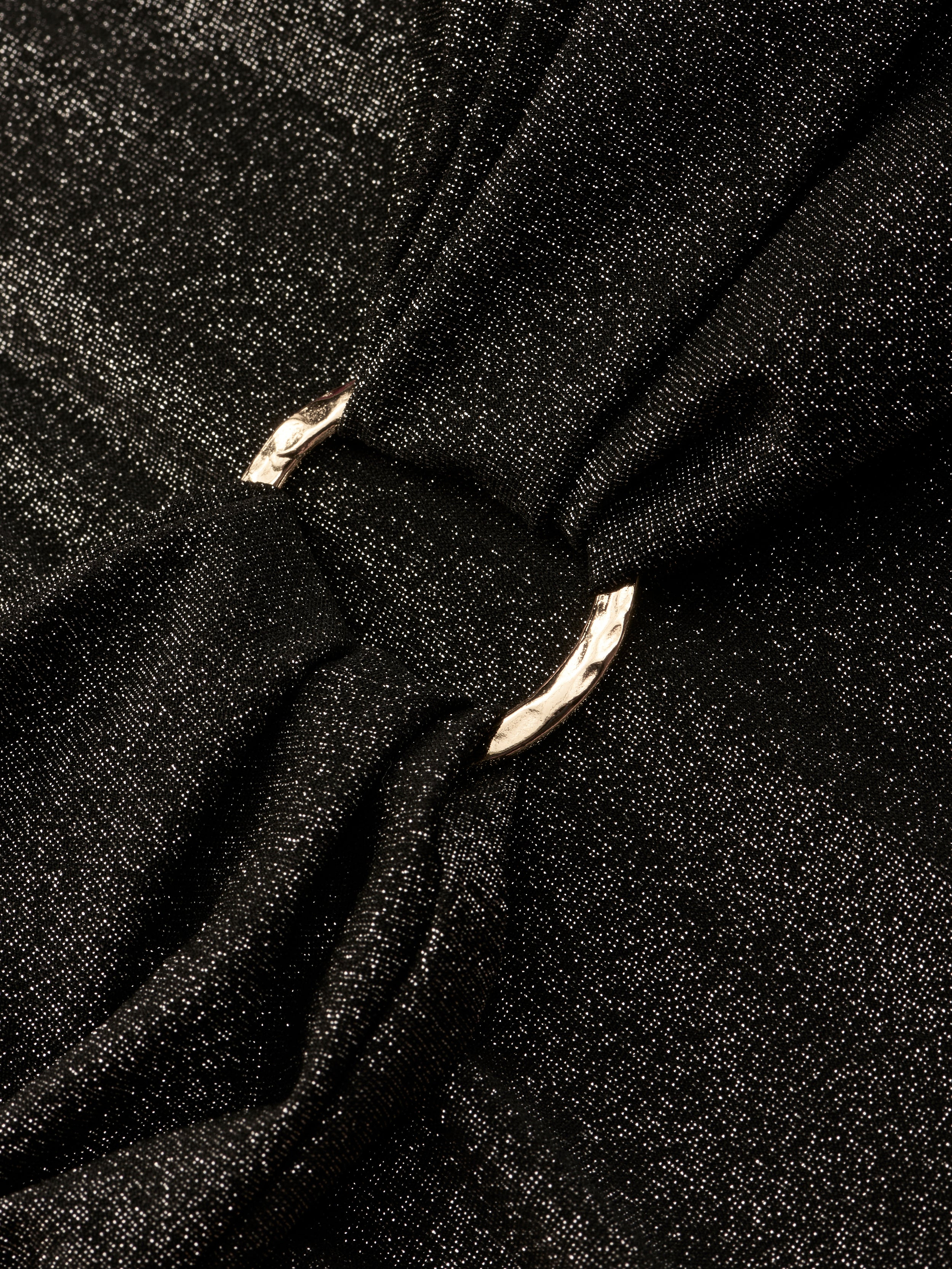 Close-up of the Lisa Plunge One-Piece Swimsuit’s shimmery black fabric, gathered by a shiny silver metal ring that creates soft folds and elegant texture.