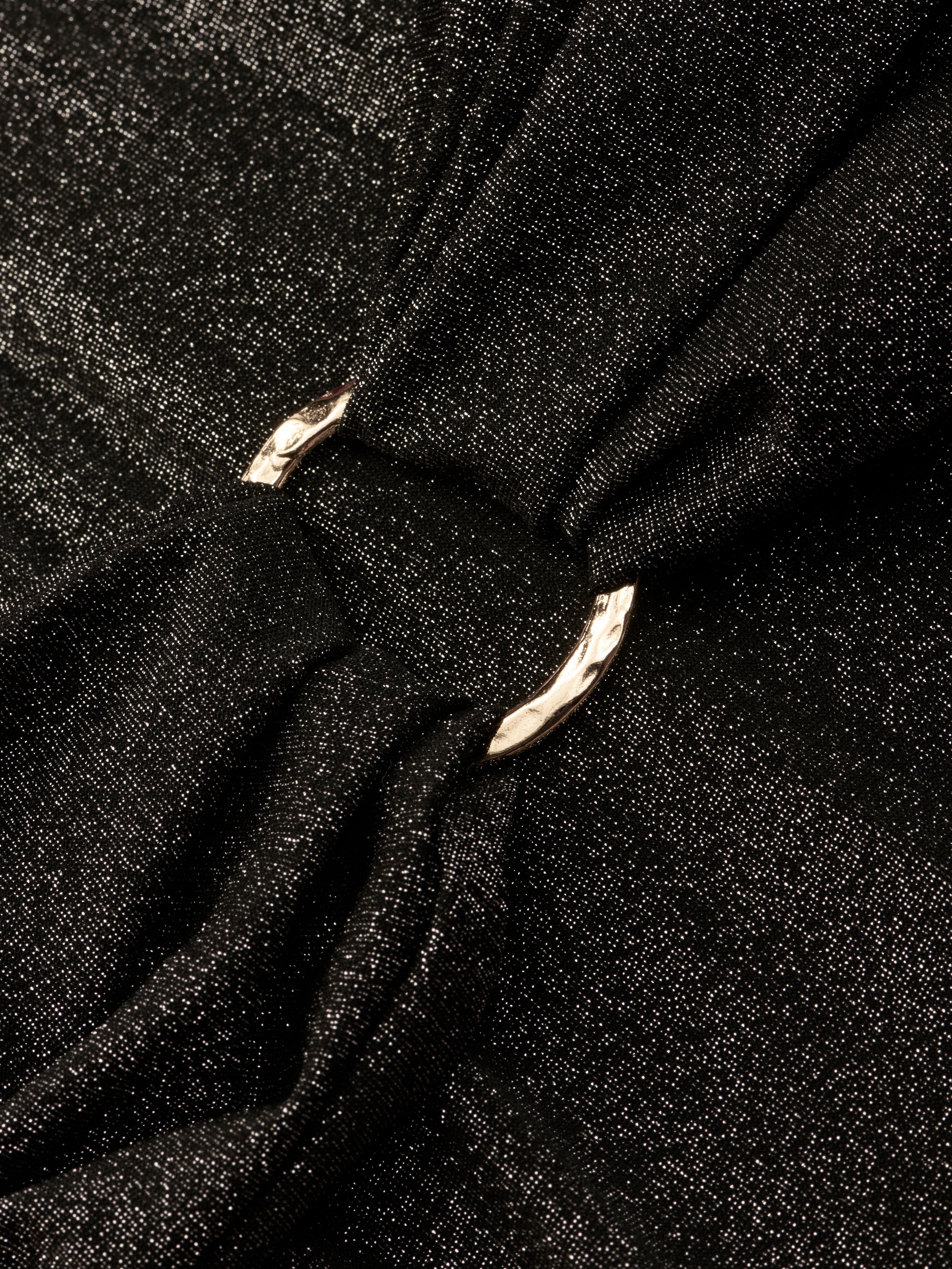 Close-up of the Lisa Plunge One-Piece Swimsuit’s shimmery black fabric, gathered by a shiny silver metal ring that creates soft folds and elegant texture.