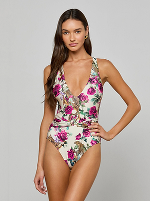 A woman with long brown hair models the Lisa Plunge One-Piece Swimsuit, featuring a vibrant rose leopard print. She stands against a plain gray background with one hand on her hip.