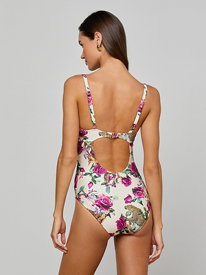 A woman faces away in the Amie Bandeau One-Piece Swimsuit, featuring pink rose and leopard print, UPF 50 protection, a low scooped back, and a cutout below the shoulder blades. The background is plain light gray.