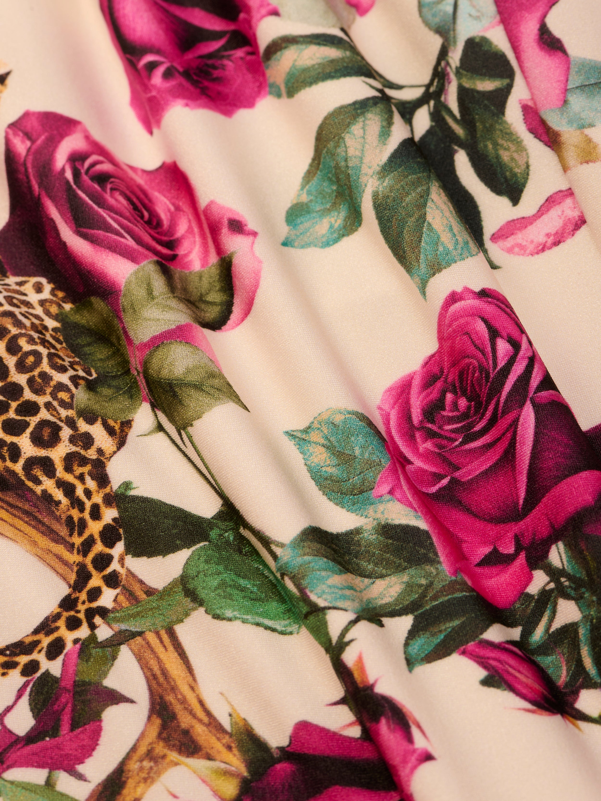 A close-up of the Amie Bandeau One-Piece Swimsuit showcases a vivid print of pink roses, green leaves, and a touch of leopard pattern on a light background.