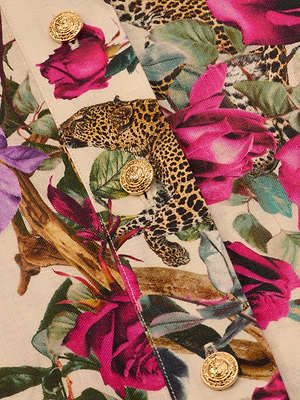 A close-up of the Hestia Cover-Up Romper, showcasing a vibrant linen design with leopards, large pink and purple flowers, green leaves, and four ornate gold buttons along the edge.
