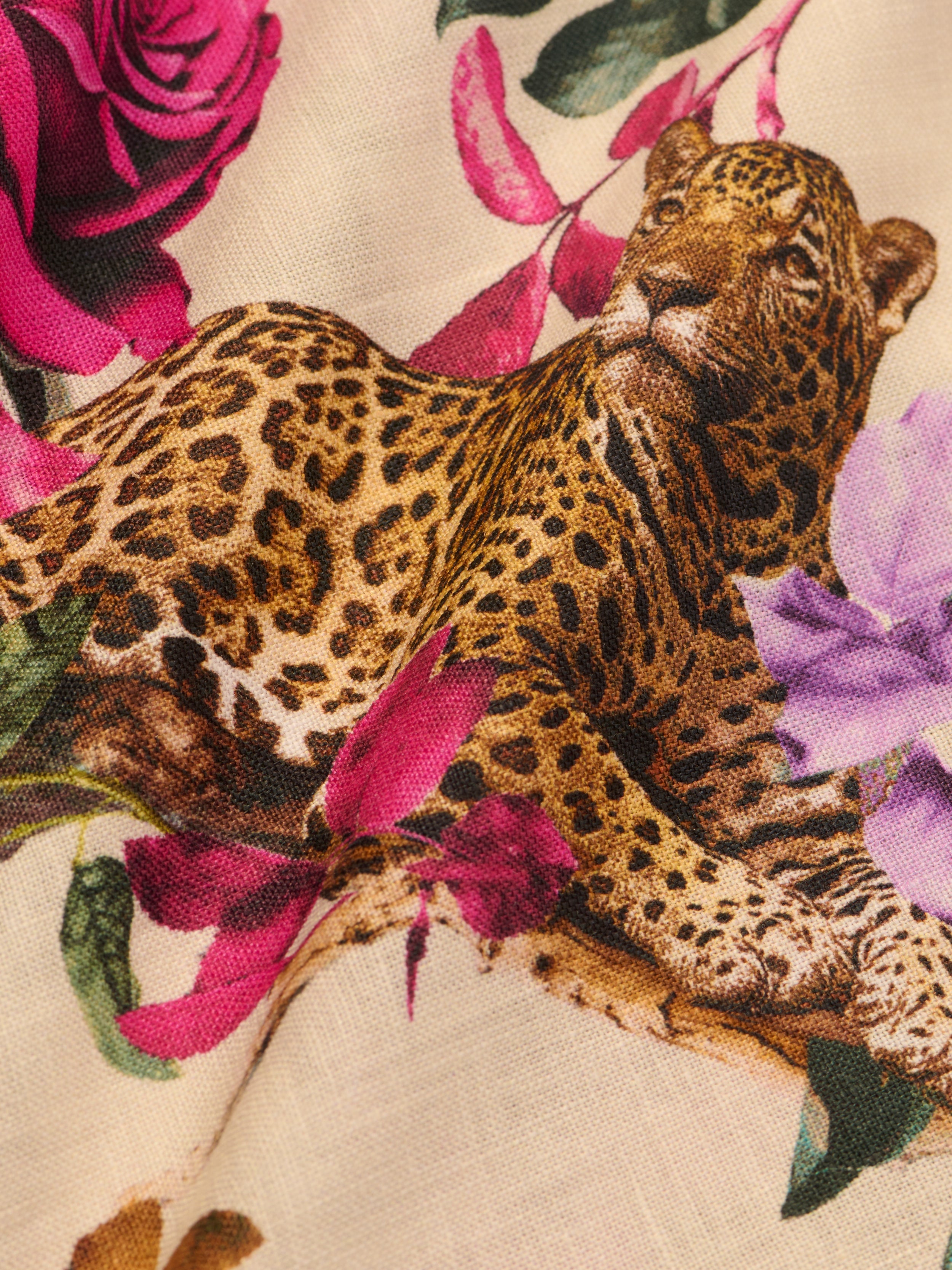 A close-up of the Geraldine Cover-Up Pant fabric, showcasing a relaxed leopard surrounded by purple and pink flowers on a beige rose leopard print background.