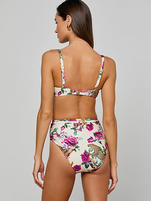 A woman with long brown hair, seen from the back, wears the Alexandria Bikini Top in a rose leopard print of pink, green, and beige. This balconette style features adjustable straps, a mid-back cut, and UPF 50 sun protection.